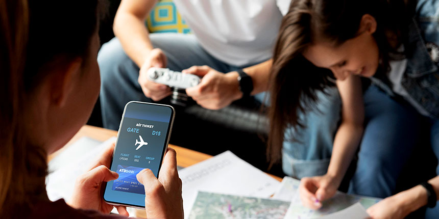Close-up of a person holding a smartphone with a digital flight ticket while friends plan a trip using maps and guides.