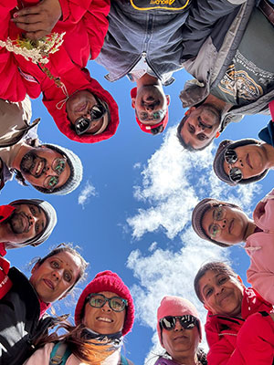 A group of friends standing in a circle looking up at the blue sky with clouds