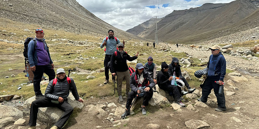 A group of pilgrims resting on rocks while trekking the sacred Mount Kailash Parikrama, surrounded by high-altitude mountains and rocky trails.