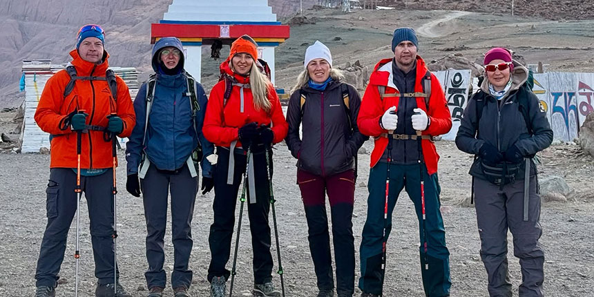 A group of trekkers in warm gear posing together during a Himalayan expedition with mountains and a stupa in the background