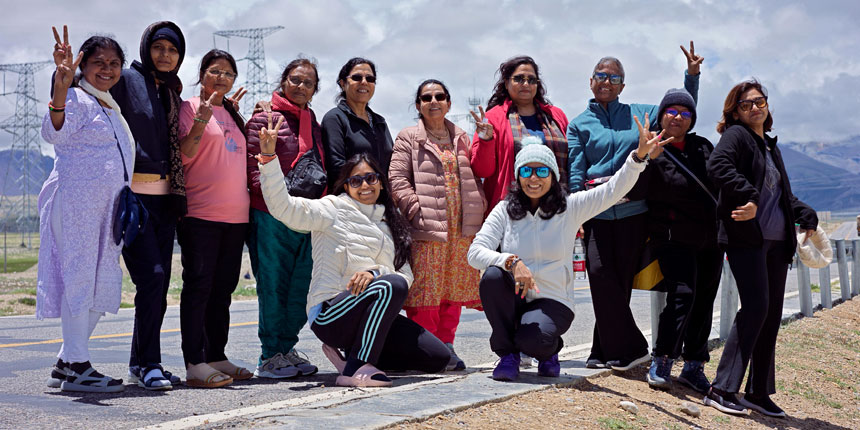 A group of smiling women travelers posing together outdoors during a road trip with kailash mansarovar yatra
