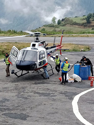 A helicopter on the helipad being refueled and prepared, with crew members assisting, used for Kailash Manasarovar Yatra travel.