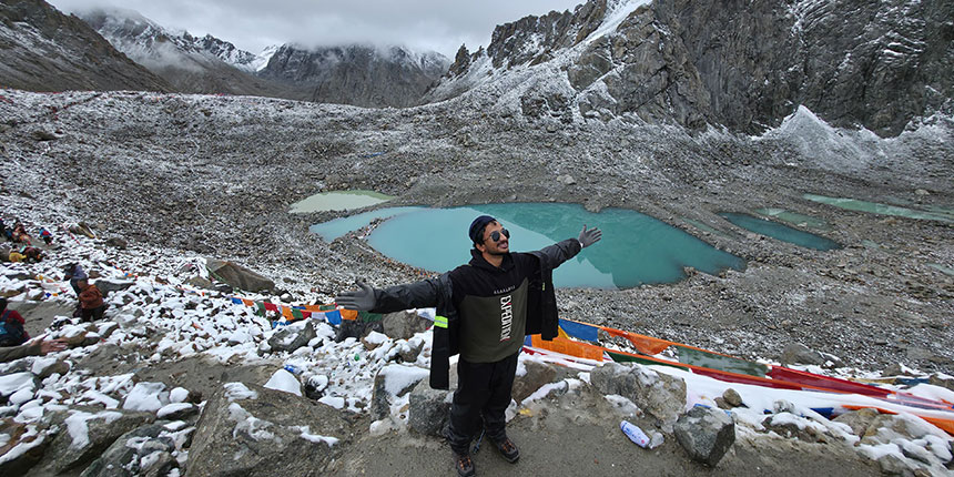 A pilgrim standing with open arms near turquoise lakes surrounded by snow-capped mountains during Mount Kailash Yatra