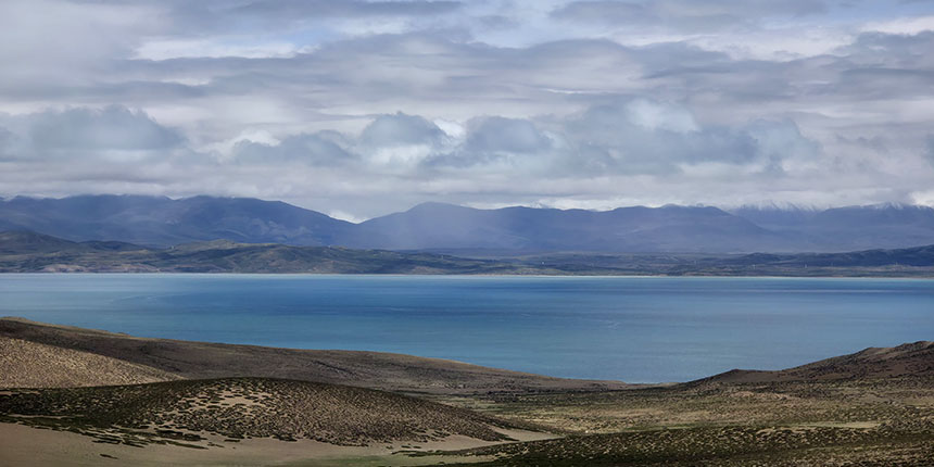 Beautiful blue lake with surrounding mountains and dramatic cloudy sky in a remote landscape