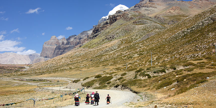 Pilgrims walking along a trail toward Mount Kailash in Tibet, with snow-capped peaks and rugged mountain terrain in the background