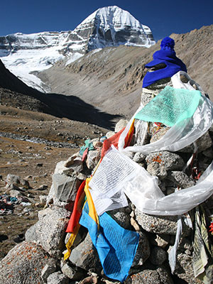 Pile of rocks with colorful Tibetan prayer flags in front of Mount Kailash, a sacred Himalayan peak in Tibet