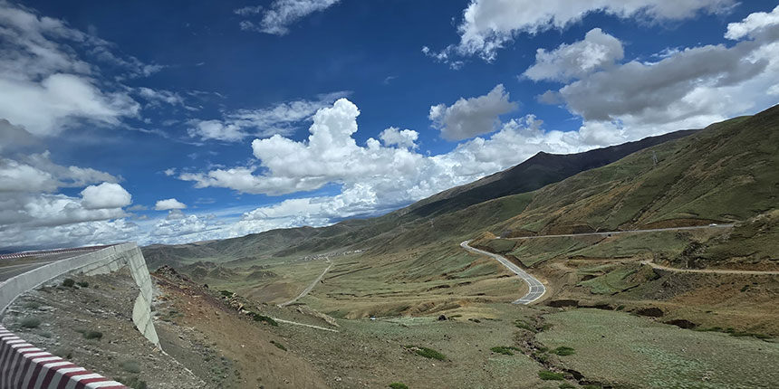 Winding road through mountains with clear blue sky and white clouds in a high-altitude Tibetan landscape