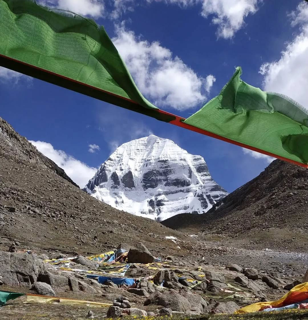 Snow-covered Mount Kailash seen through fluttering Tibetan prayer flags on a clear day during a sacred Himalayan pilgrimage