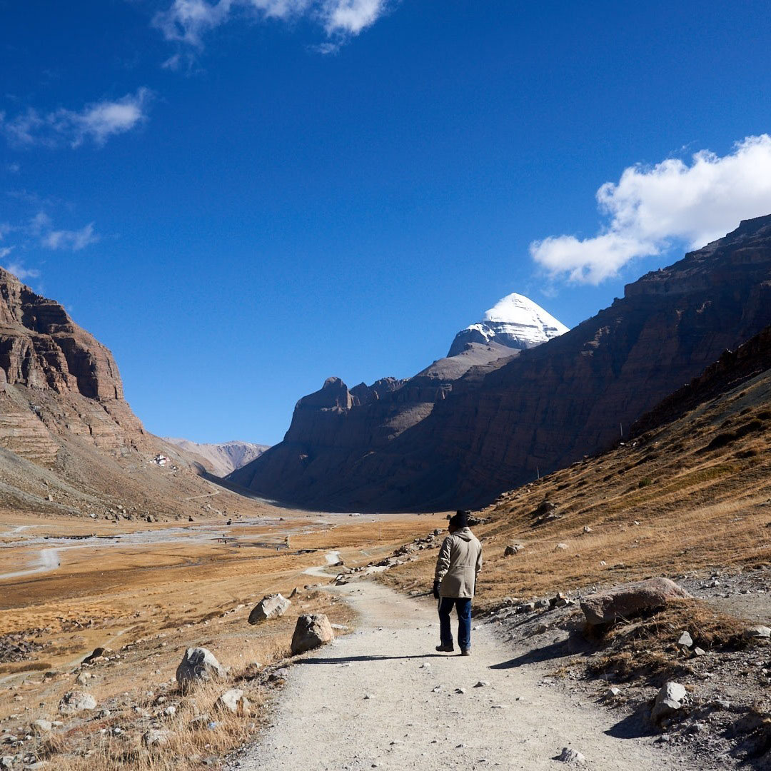 Solo trekker walking towards Mount Kailash on a clear day, surrounded by rugged Himalayan terrain in Tibet