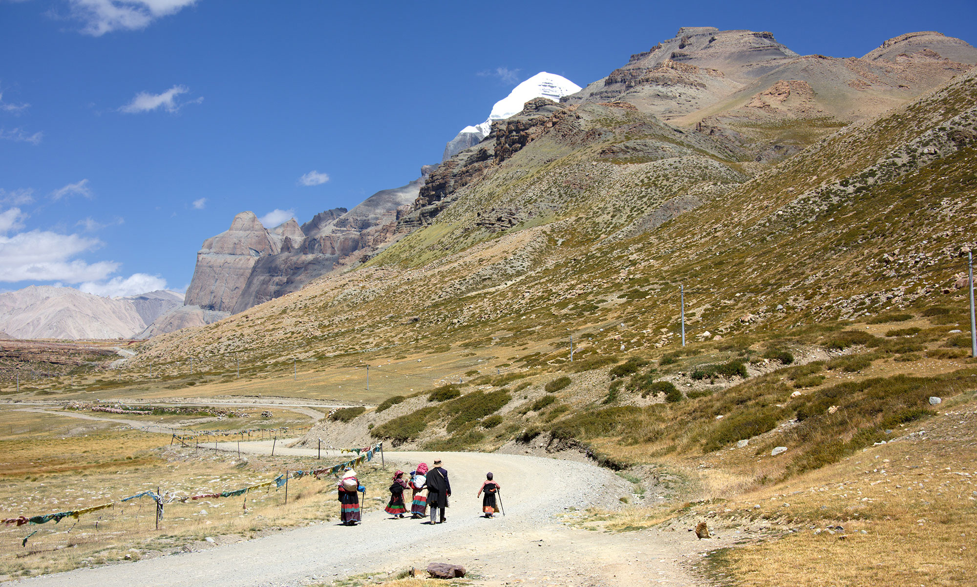 Group of pilgrims walking on the trekking path towards Mount Kailash with snow-capped peak and rocky mountains in the background during Kailash Mansarovar Yatra